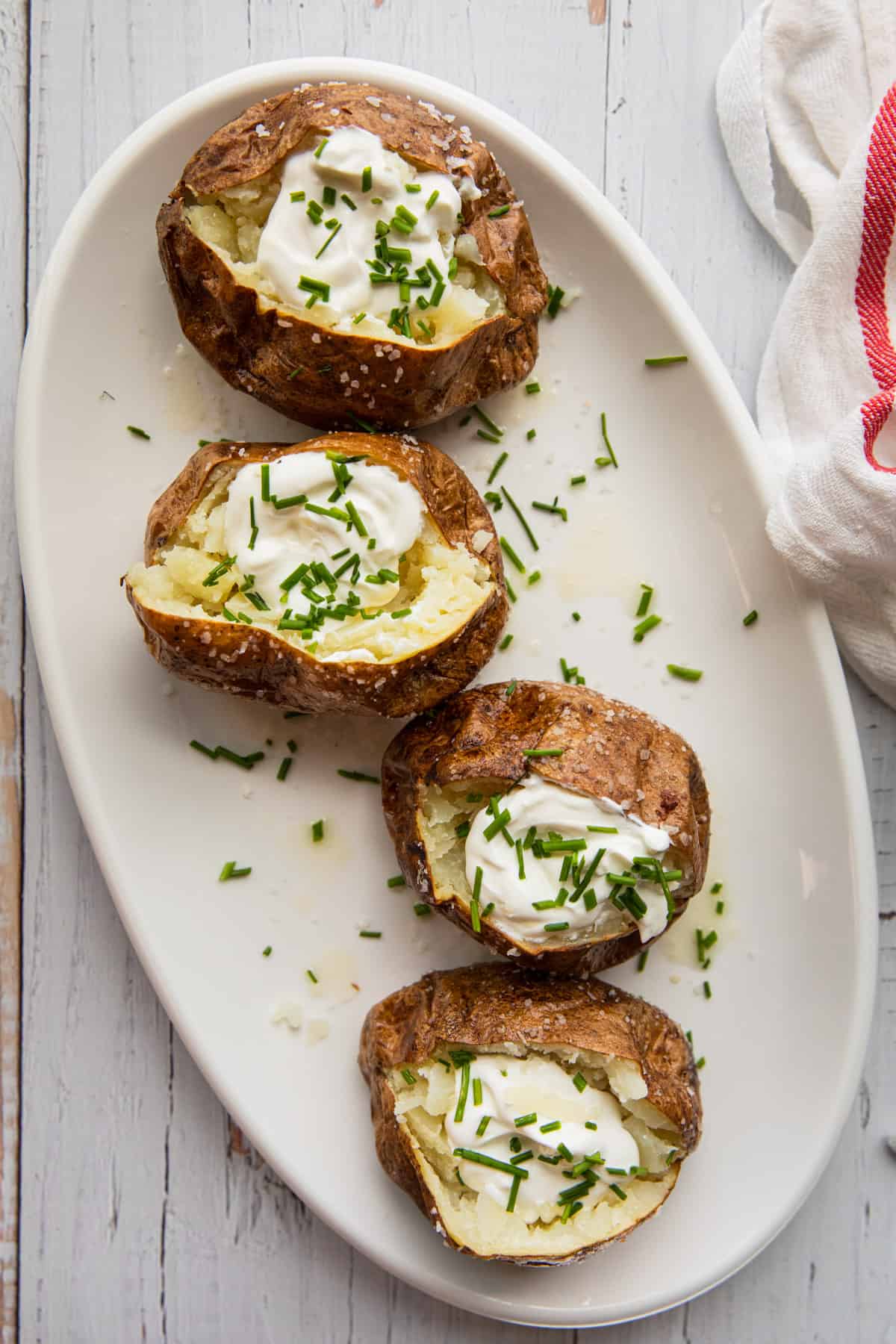 a white platter with 4 baked potatoes topped with sour cream and chives