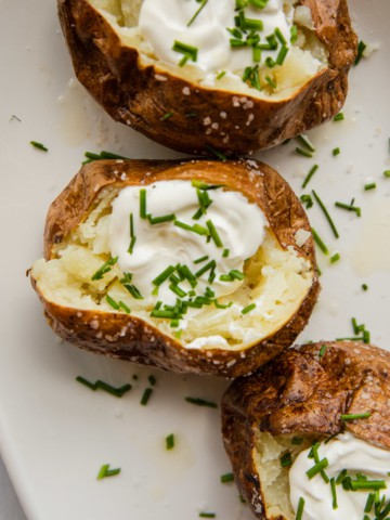 baked potatoes with sour cream and chives on a white platter