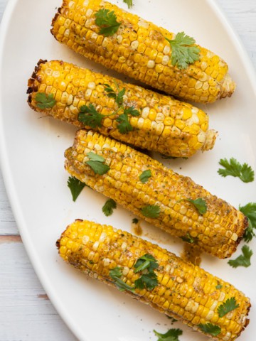 a platter of corn on the cob with cilantro ganish