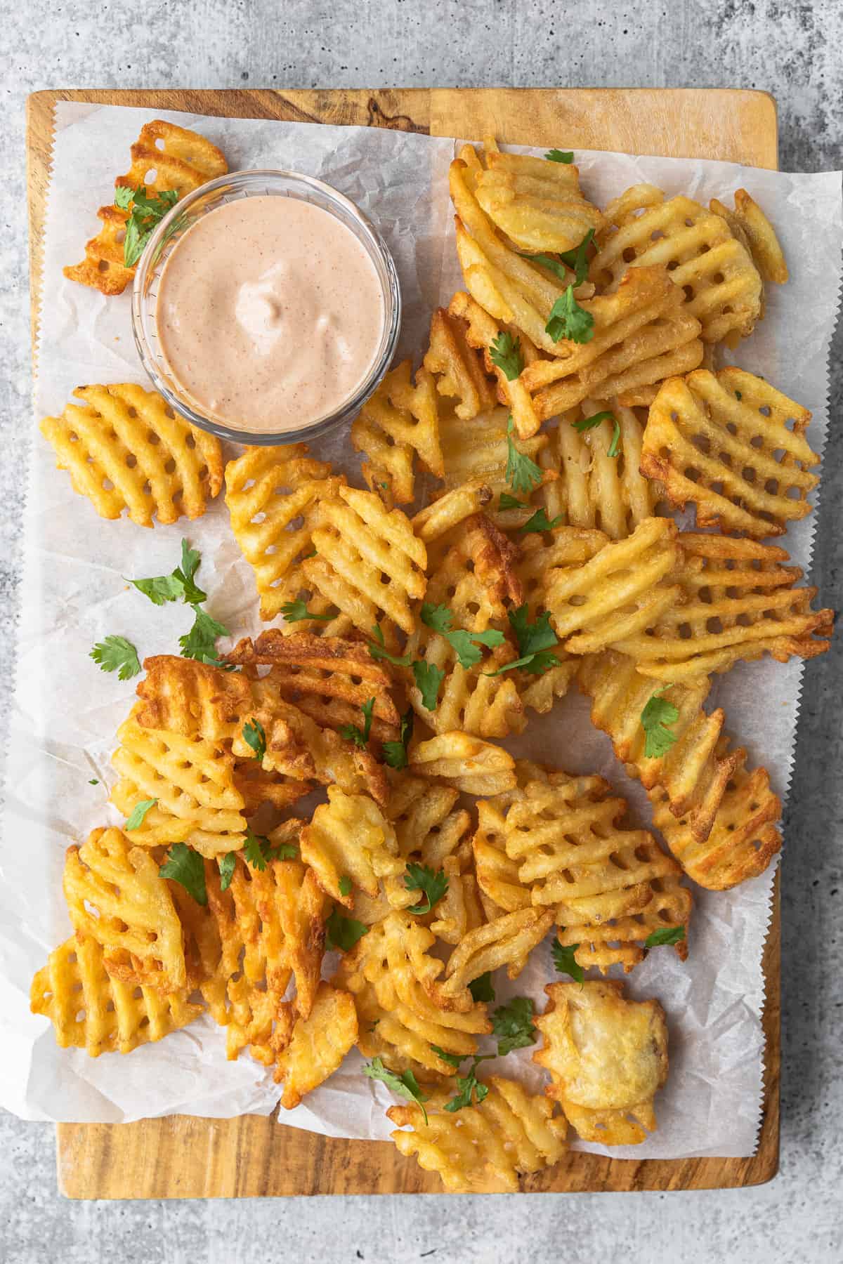waffle fries on a cutting board with parchment paper and a pink dipping sauce