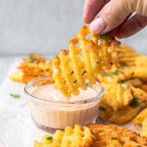 dipping a waffle fry into a pink sauce