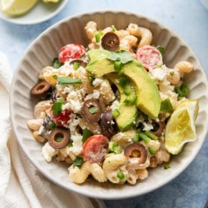 a bowl of corn and black bean pasta salad with lime wedges