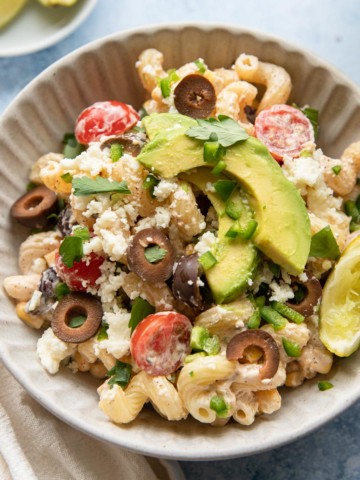 a bowl of corn and black bean pasta salad with lime wedges