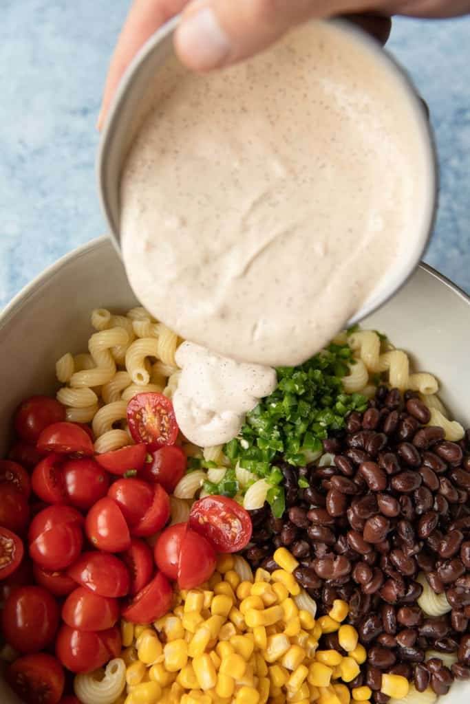 pouring a creamy dressing into a pasta salad bowl