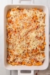 a casserole dish being layered with pasta, sauce, and cheese