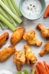 wing on a parchement paper with celery sticks, carrot sticks, and dip