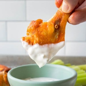 a buffalo chicken wing drum being dipped in a white dressing