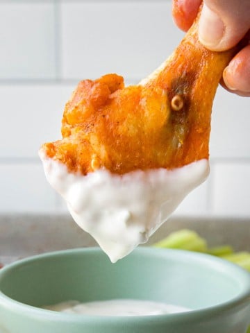 a buffalo chicken wing drum being dipped in a white dressing