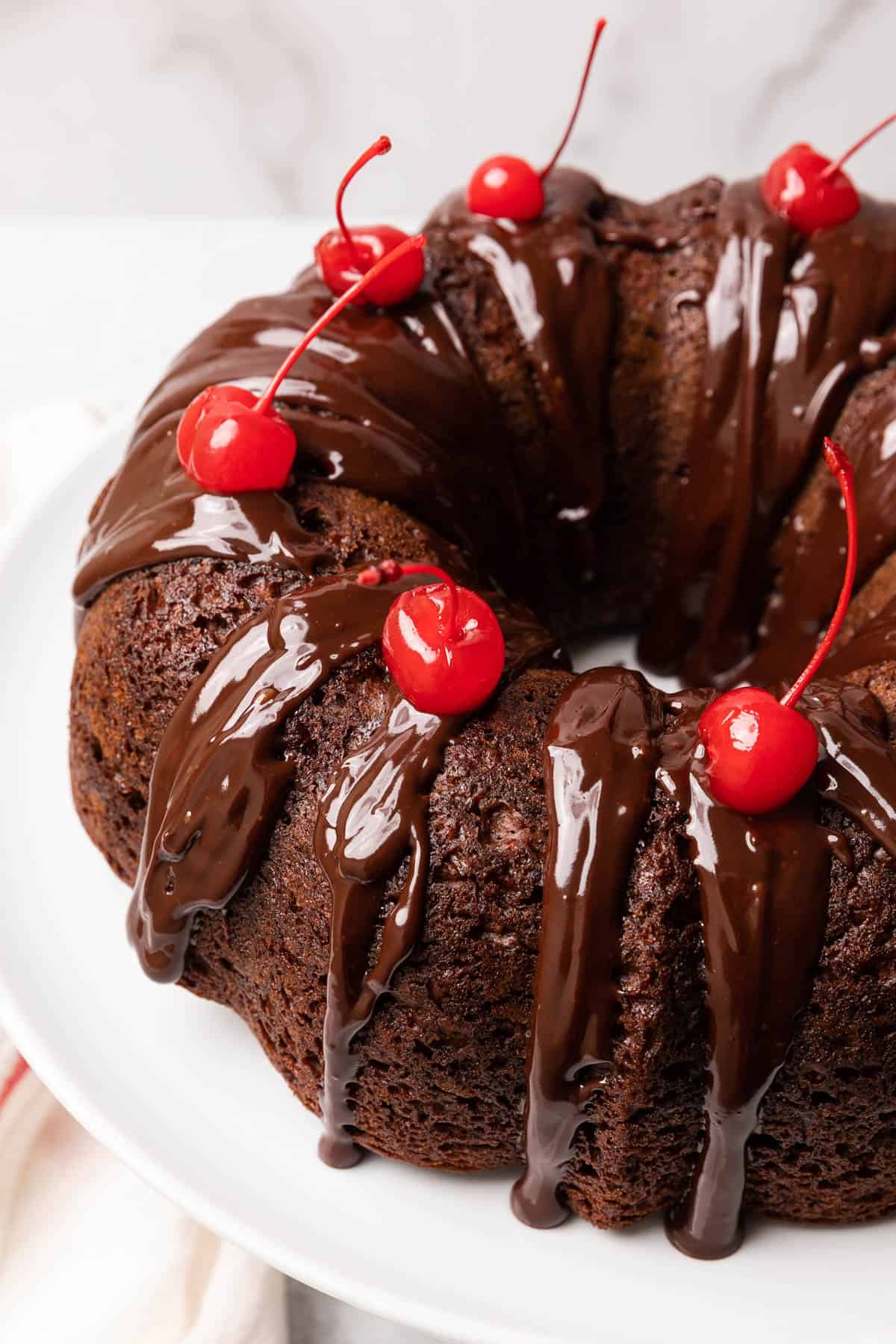 chocolate bundt cake topped with cherries on a white cake stand