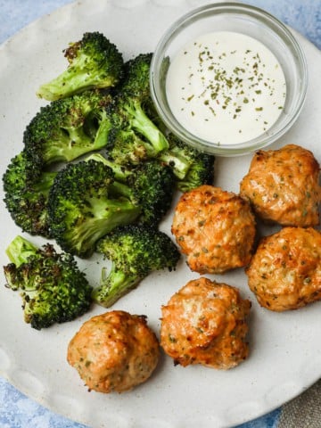 a plate of meatballs, broccoli, and a white dip