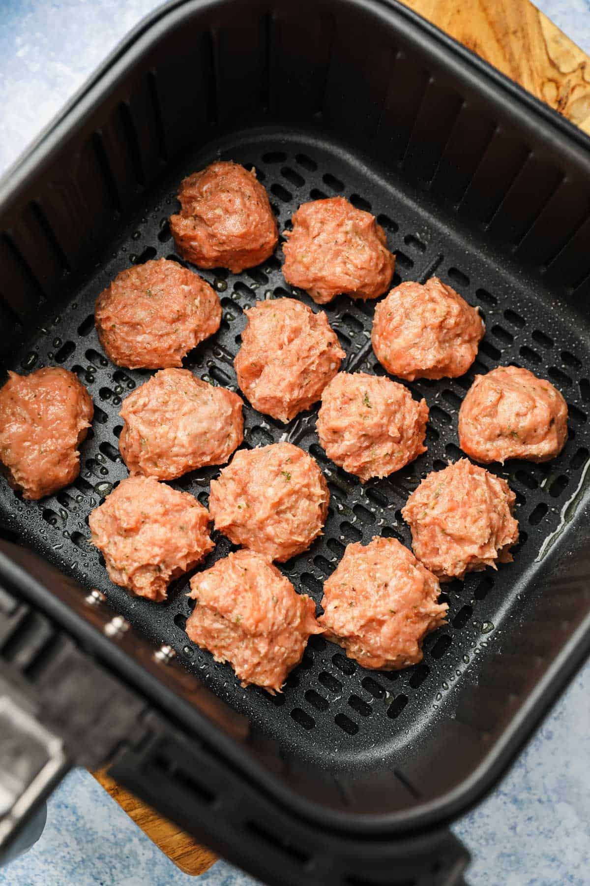 Uncooked meatballs in an air fryer basket.