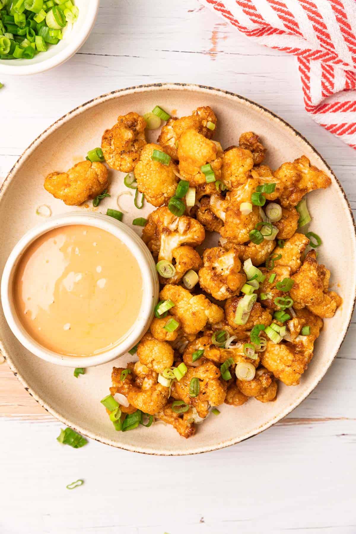 a plate of air fried cauliflower with a dipping sauce on the side