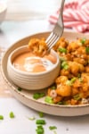 a pice of cauliflower on the end of fork going into a bowl of dip