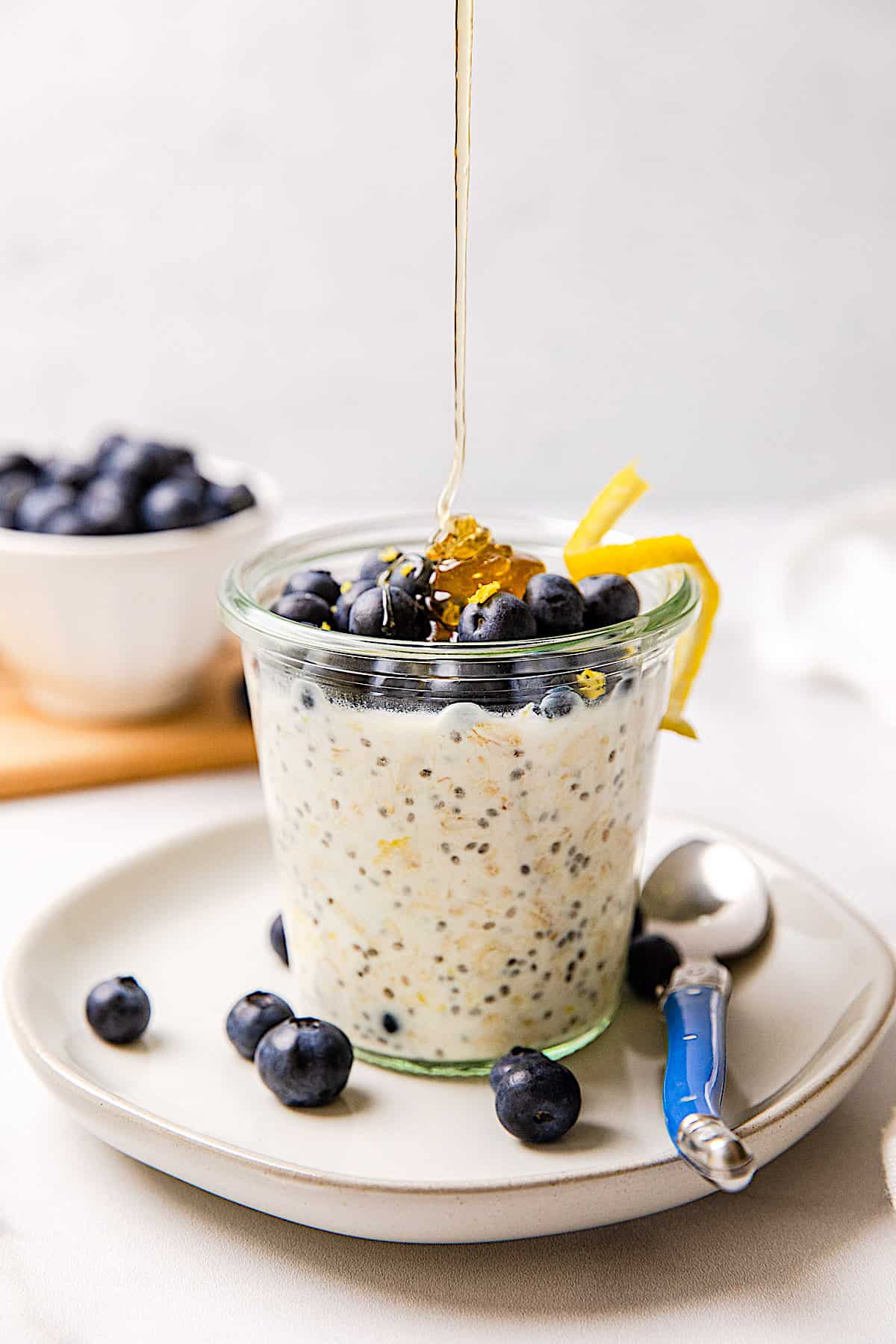 honey pouring into a glass of overnight oats topped with blueberries