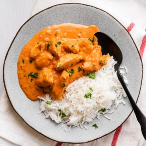 a plate of chicken in a orange sauce with rice and a spoon