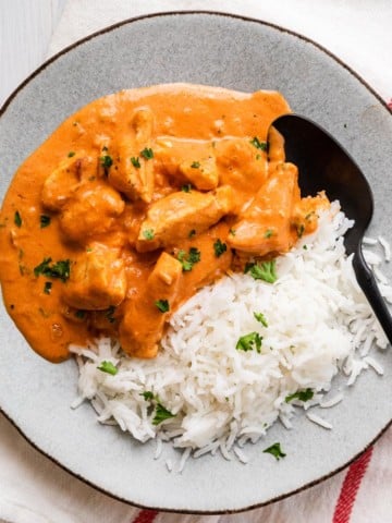 a plate of chicken in a orange sauce with rice and a spoon