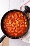 a skillet of chicken pieces cooking in a tomato sauce