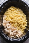 cooked pasta added to a crockpot with shredded chicken