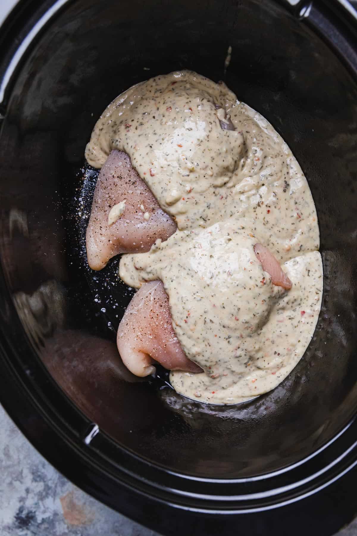 uncooked chicken breasts with sauce poured over