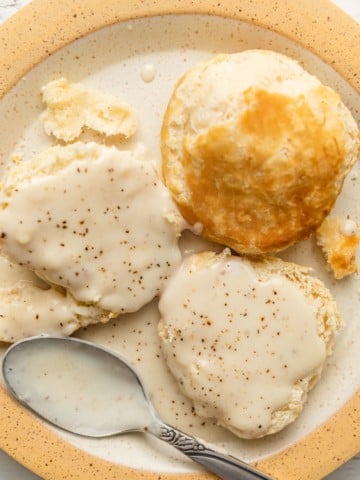 a plate of biscuits smothered in white bacon cream gravy