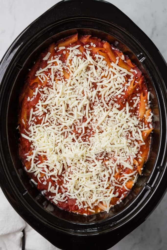 Shredded mozzarella cheese on top of a baked ziti in a crockpot