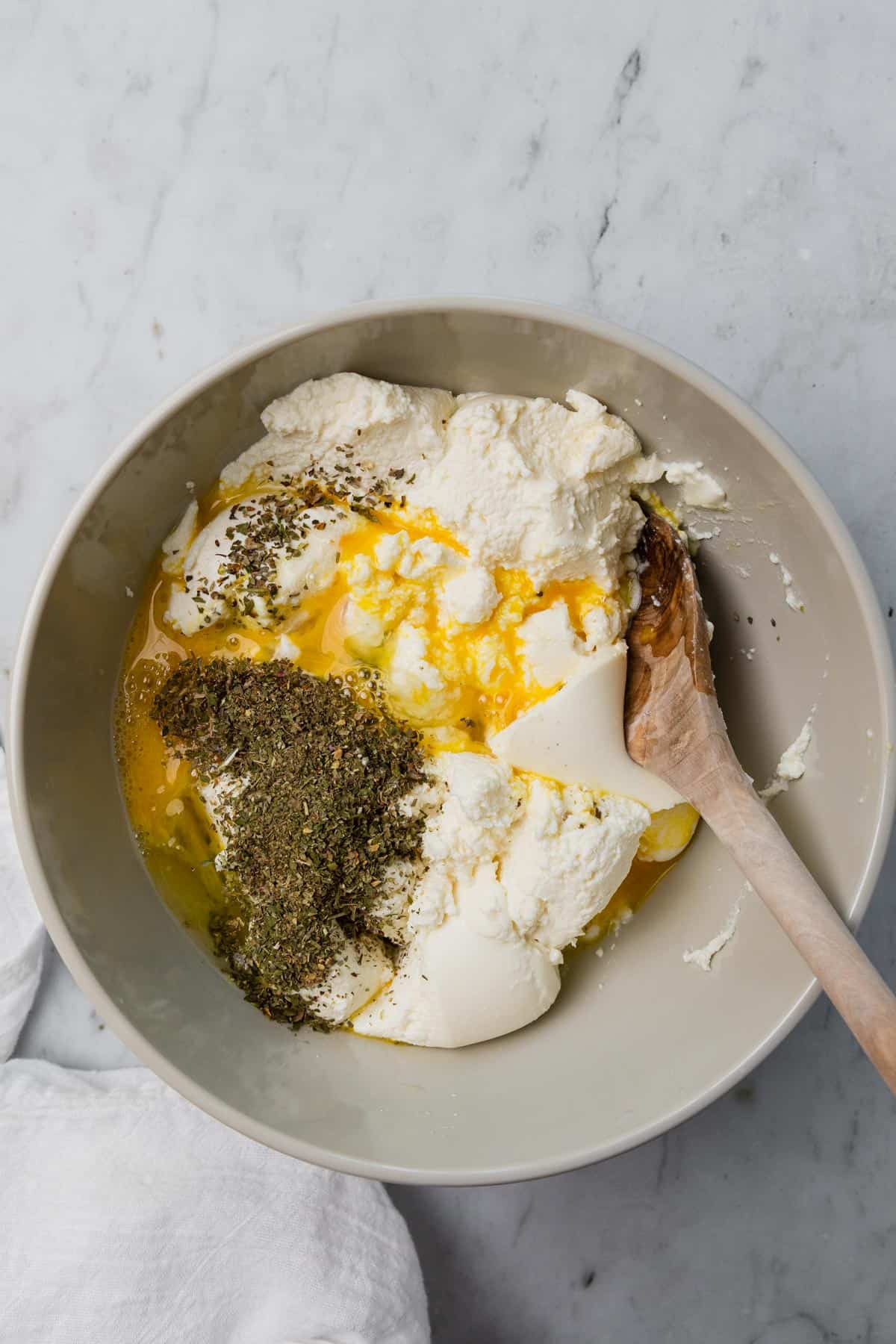 ricotta cheese, eggs and herbs in a mixing bowl