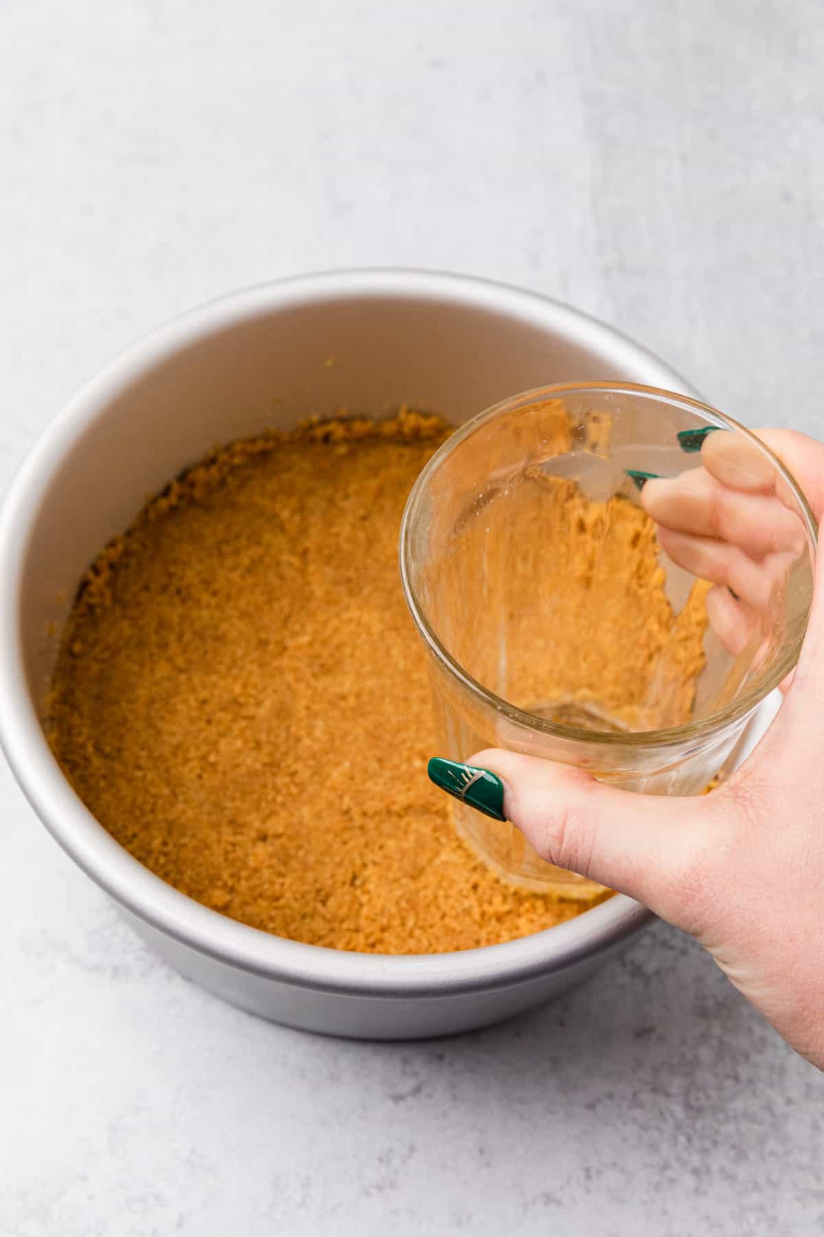 a glass pressing crumbs into a pan