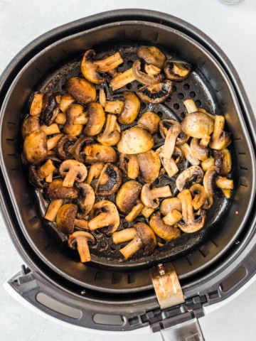 an air fryer basket with cooked mushroom slices
