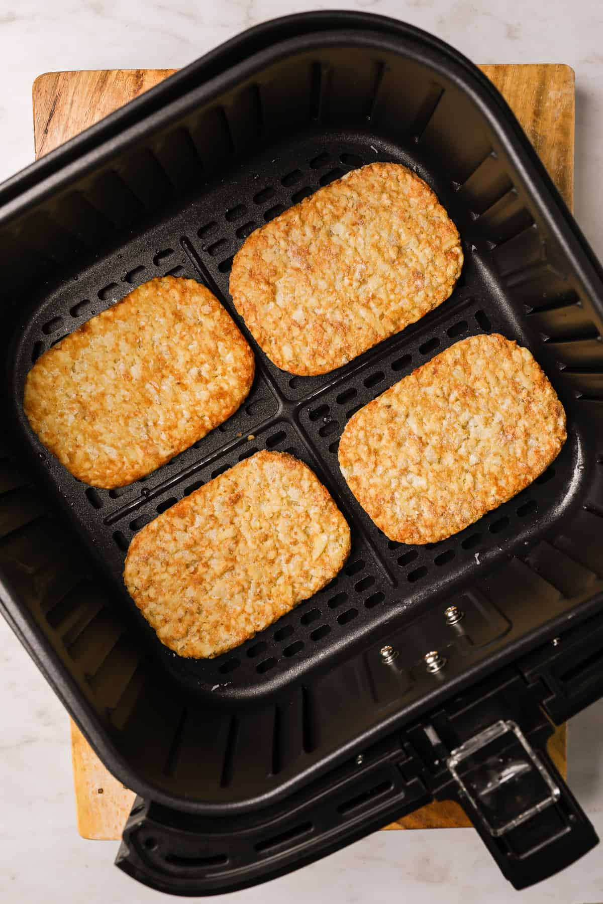 Four hash brown patties in an air fryer basket.