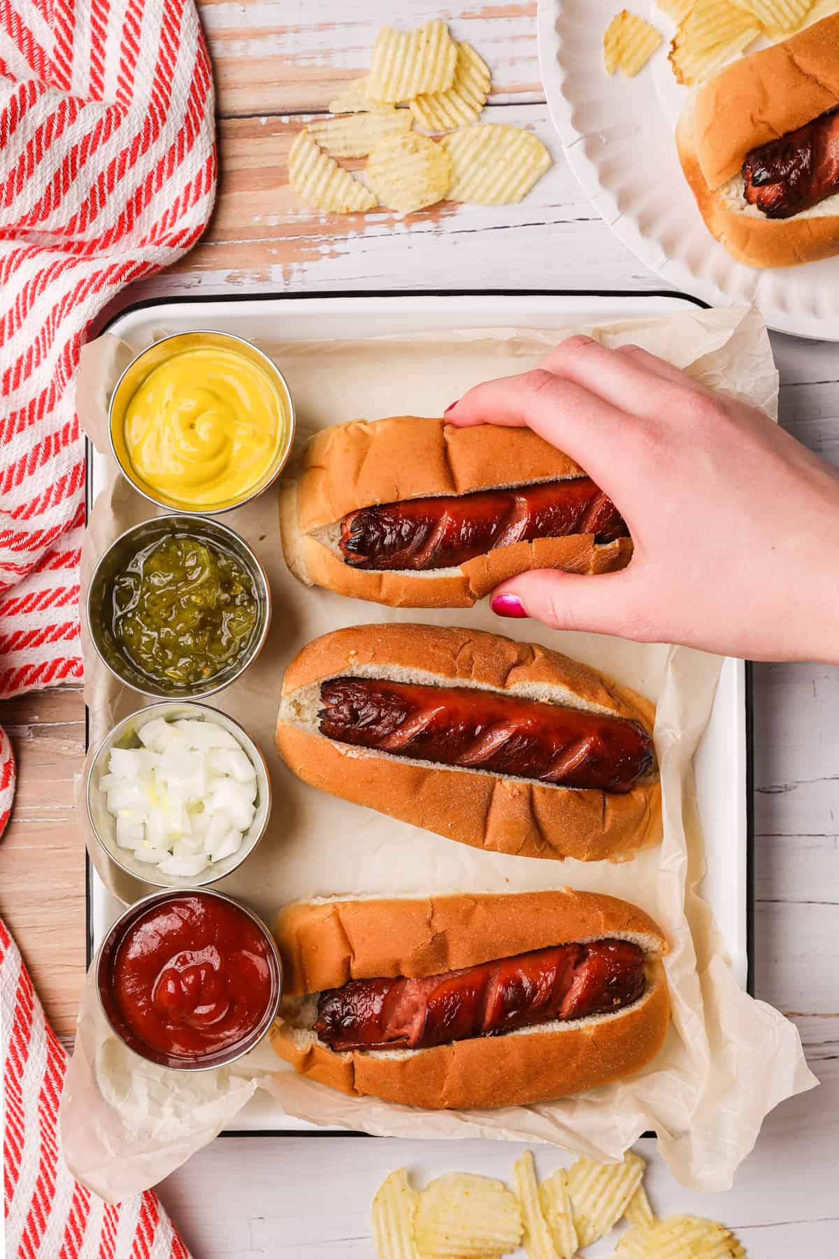 a hand taking a hot dog from a platter