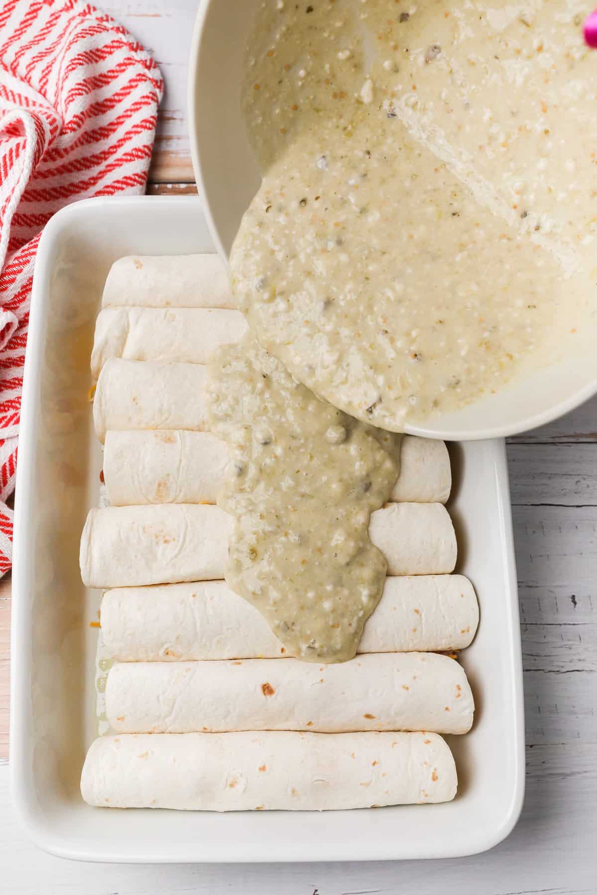 pouring sauce over rolled enchiladas