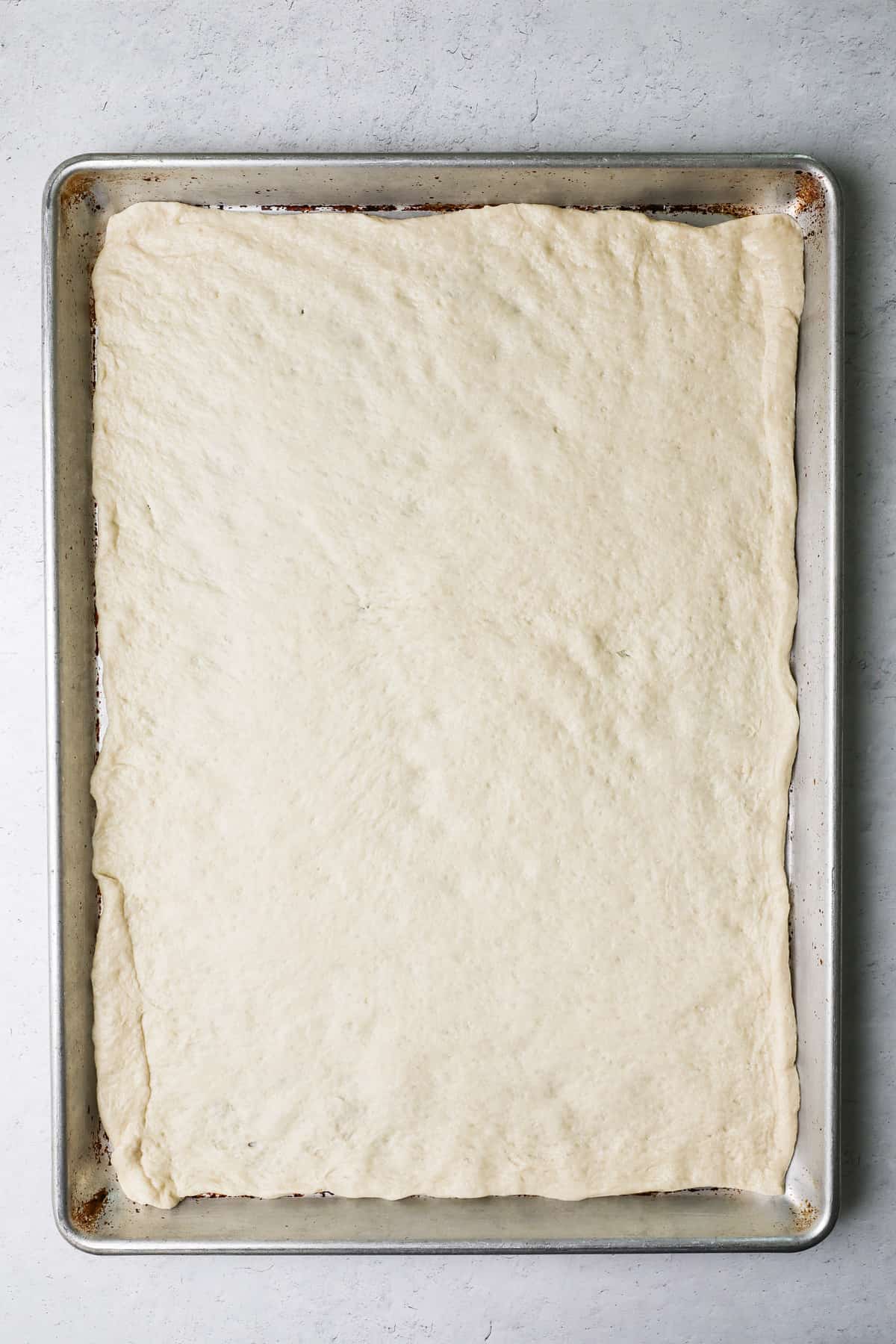 A pizza crust spread on a baking pan.