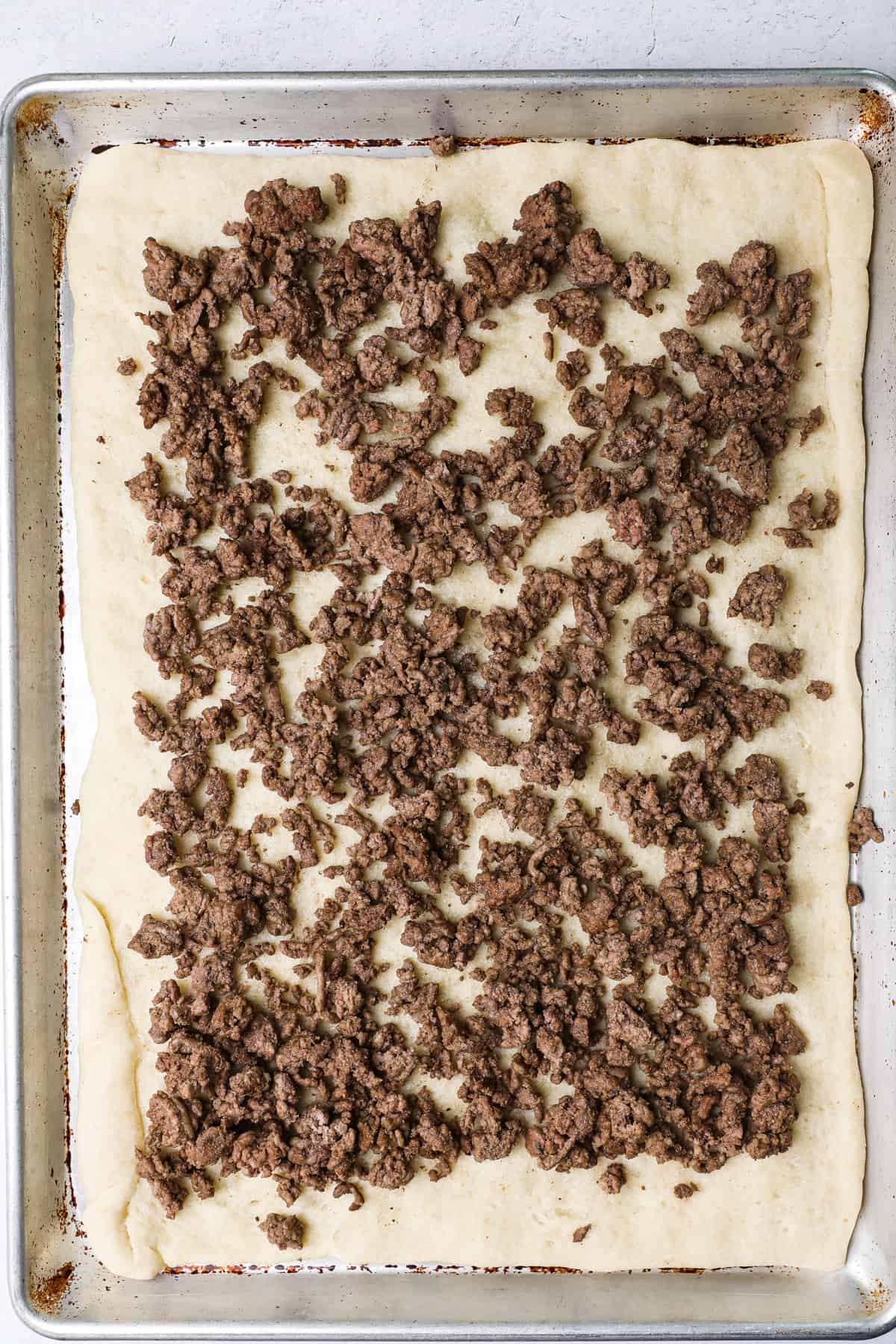 Cooked ground beef spread on a pizza crust.