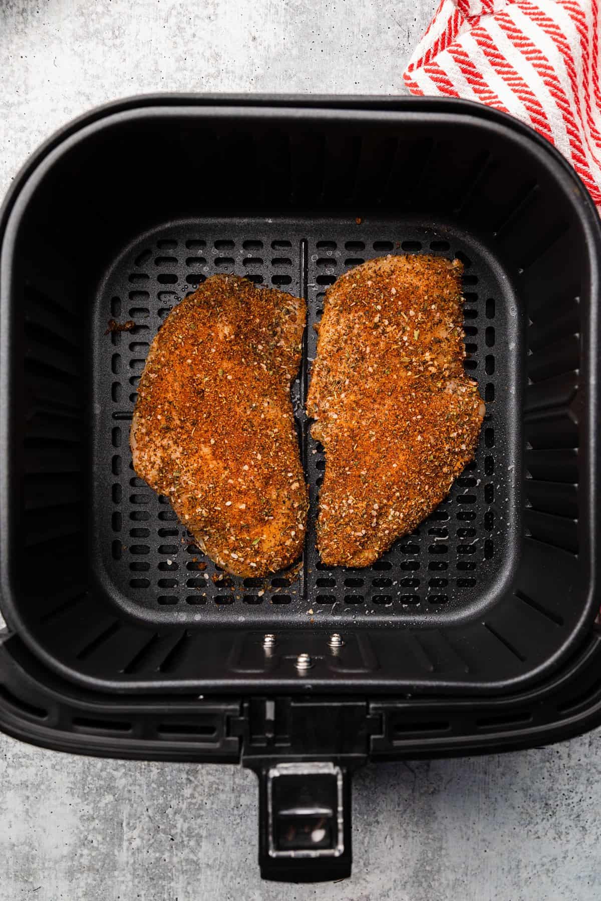 seasoned chicken in air fryer basket.