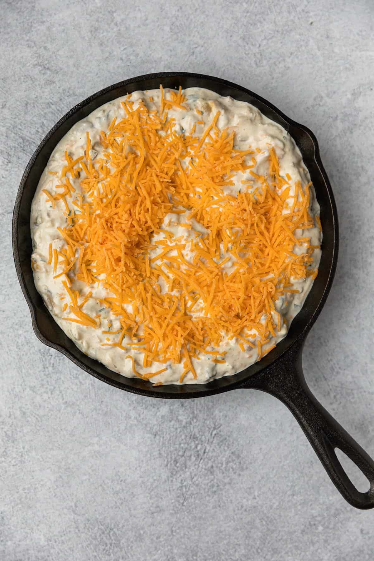 adding shredded cheese to the top of the green chile dip before baking it