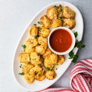 a white platter of breaded air fryer tortellini with marinara saucer on the side