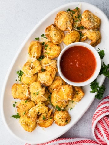 a white platter of breaded air fryer tortellini with marinara saucer on the side