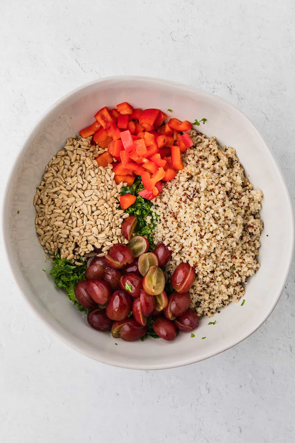 a bowl with salad ingredients: quinoa, grapes, sunflower seeds, kale, red pepper