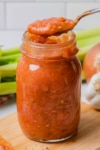 the completed tomato sauce in a jar with a spoon