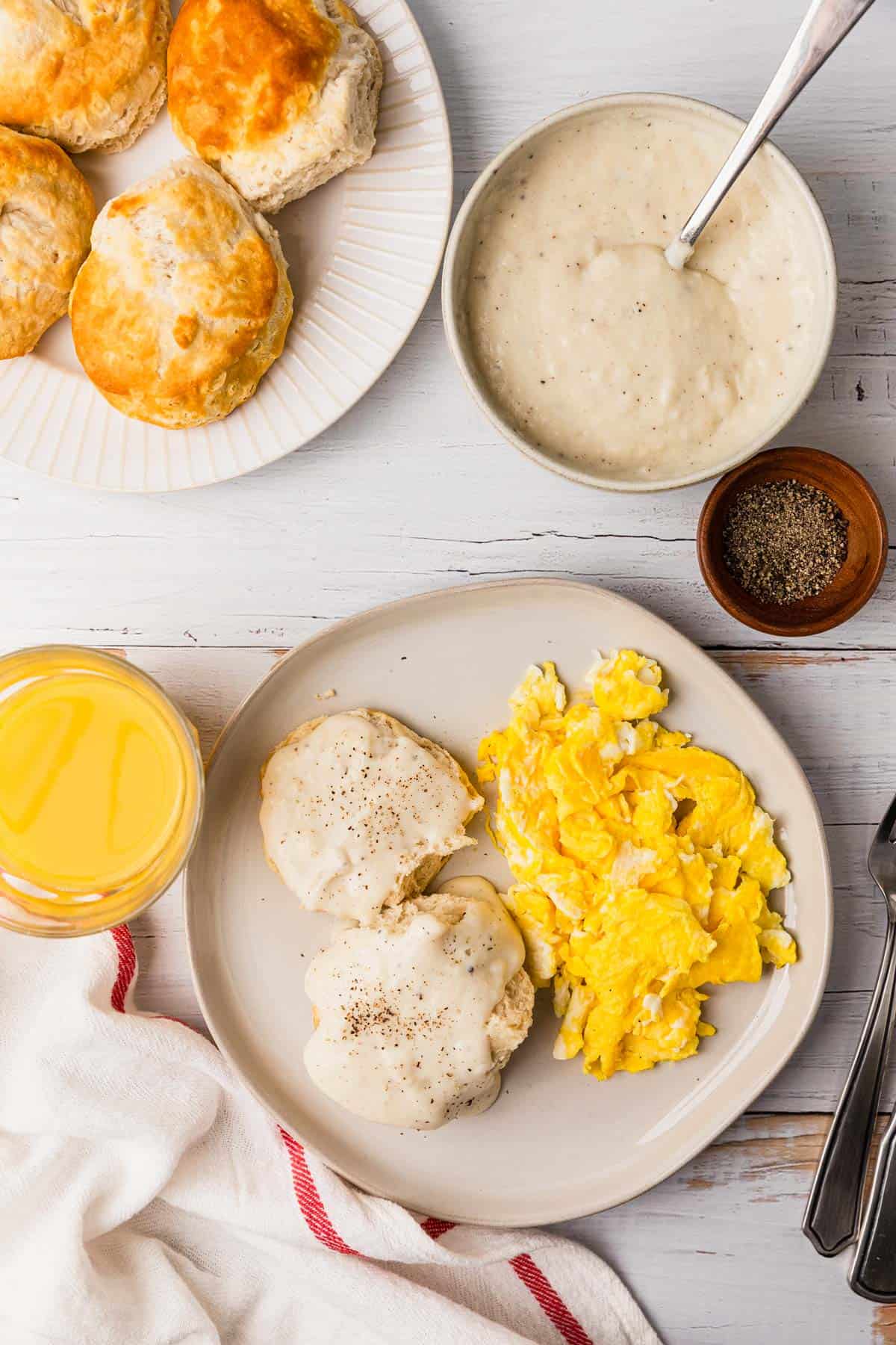 a table of biscuits covered in a white gravy with a side of eggs