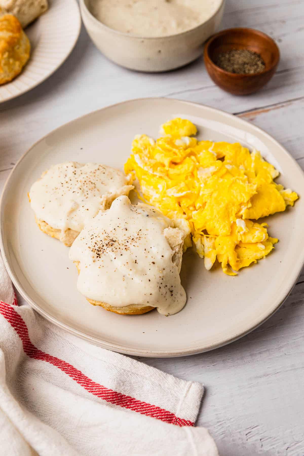 a plate with a breakfast meal of biscuits, gravy, and scrambled eggs