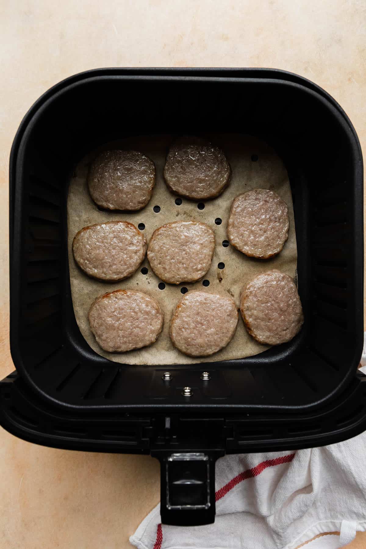 halfway cooked sausage patties in an air fryer basket