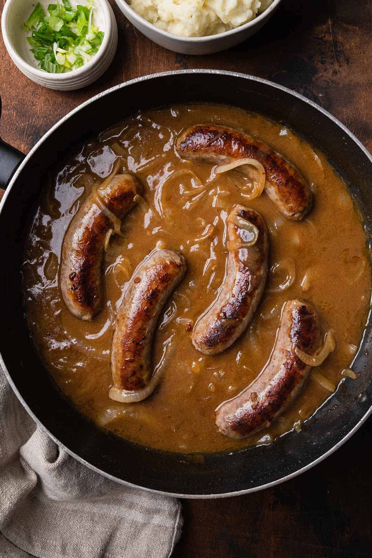 a pan of sausages simmering in stout gravy with onions