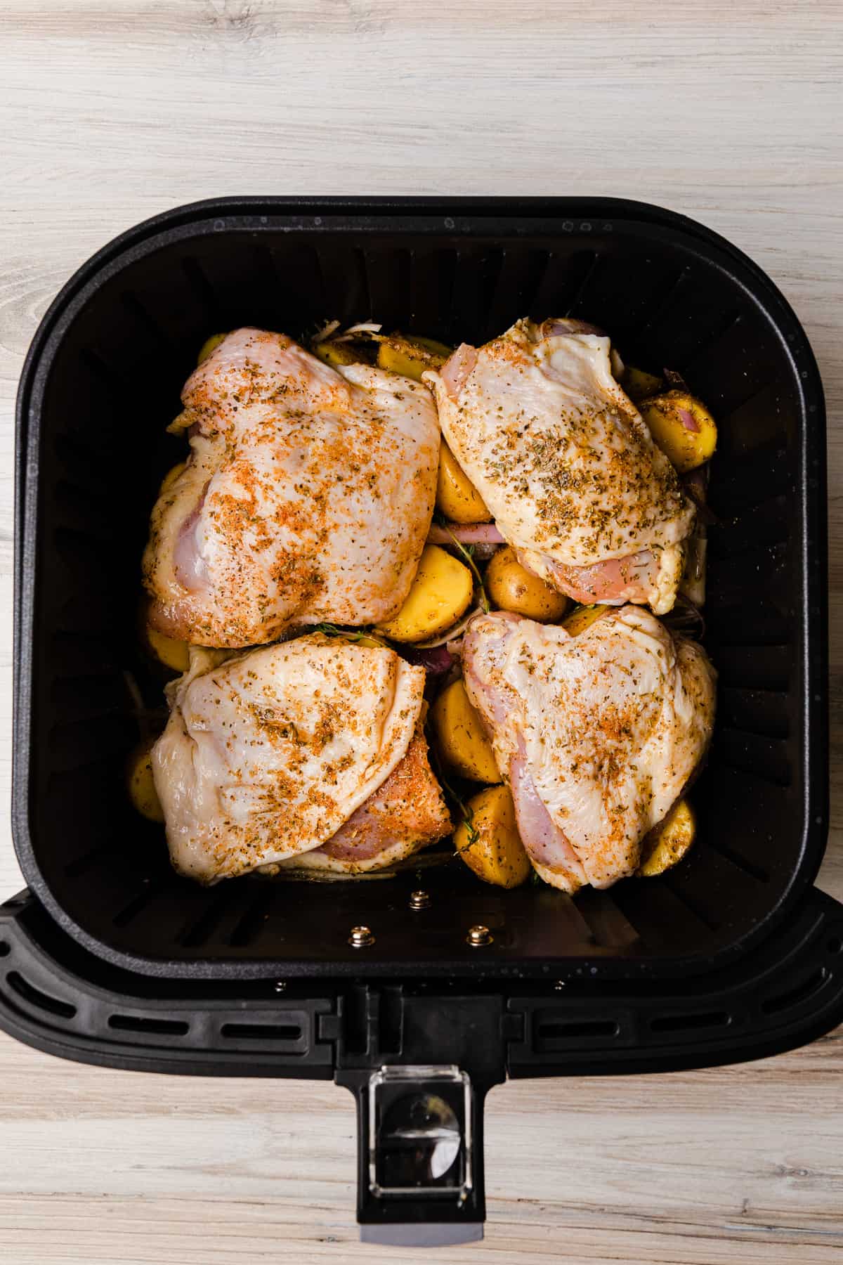 Adding seasoned chicken to the air fryer basket on top of the potatoes.