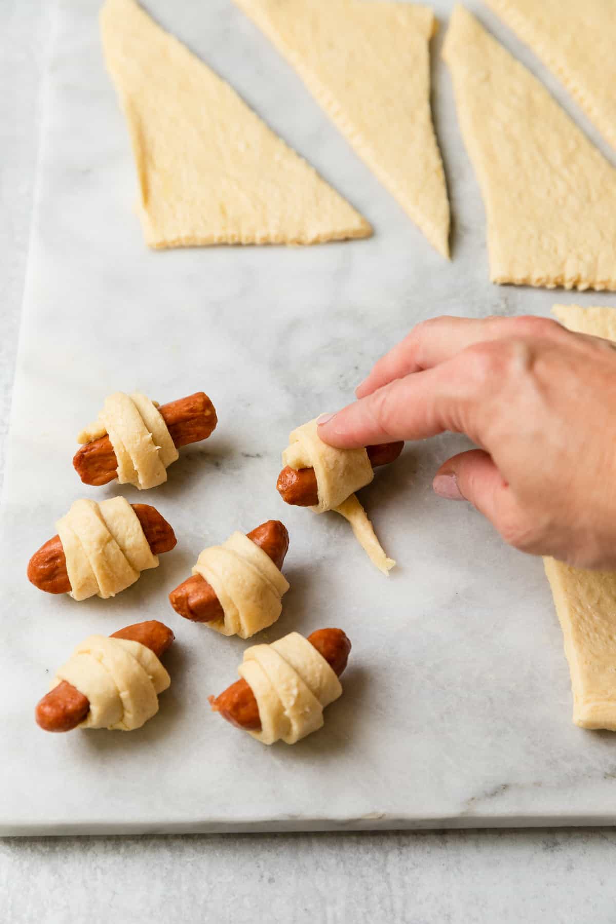 Making the recipe by rolling the sausages in the strips.