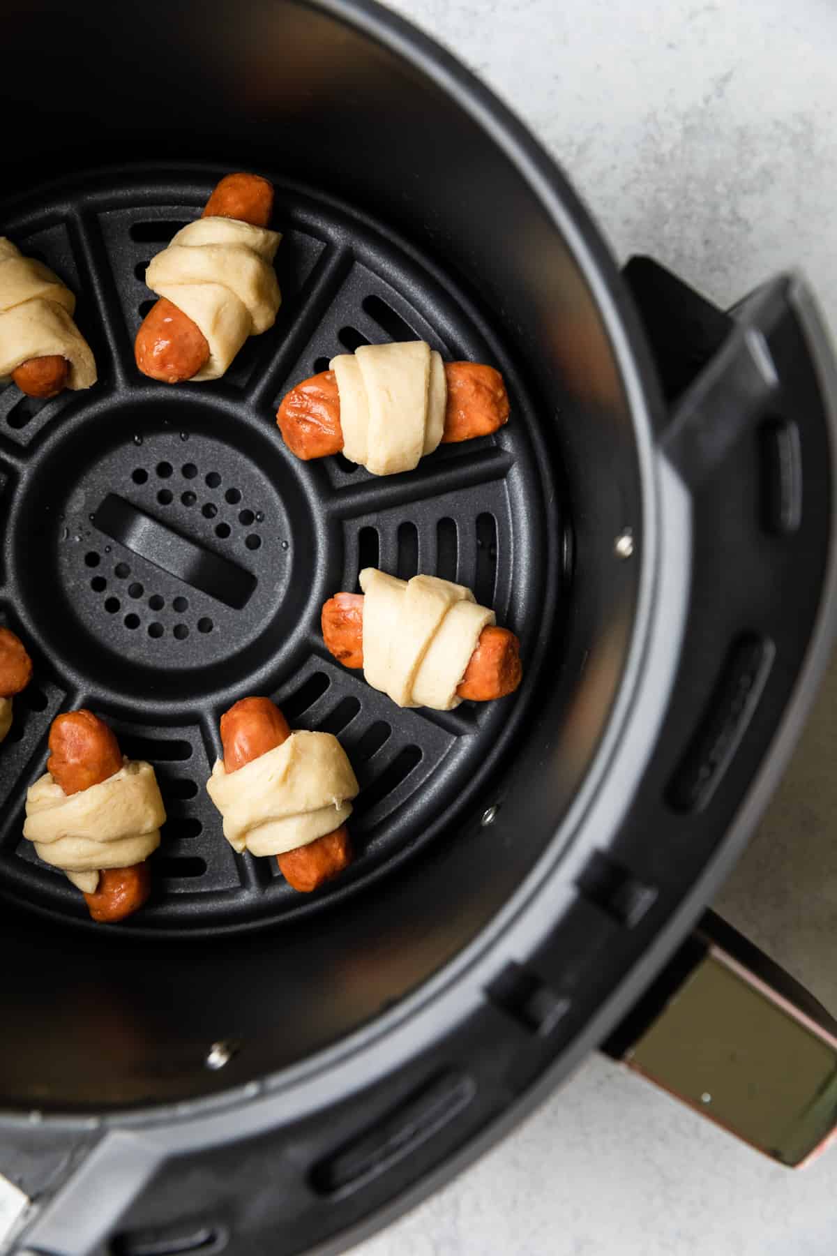 Process image of uncooked pigs in a blanket in the air fryer basket.