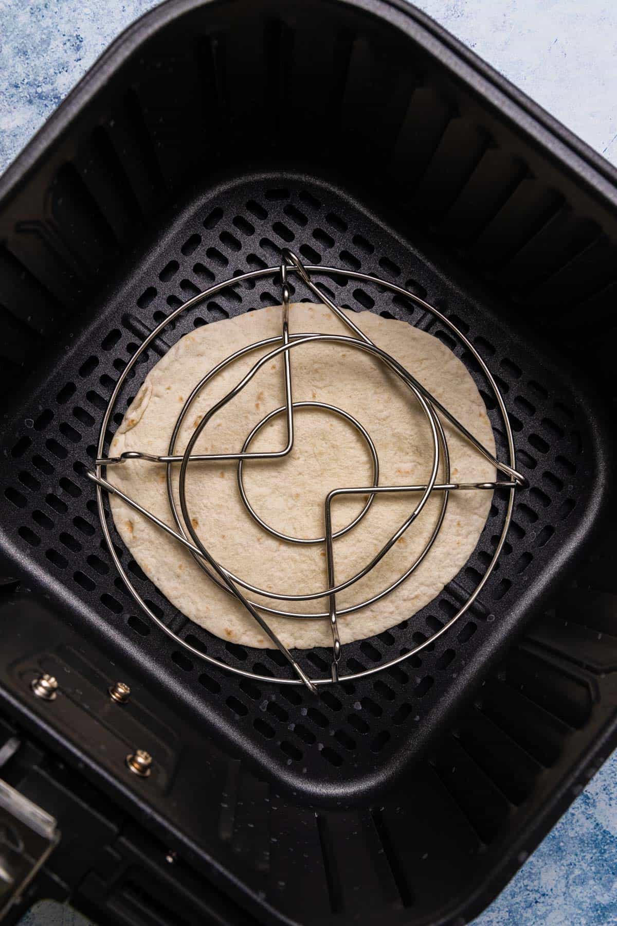 making the tostada in the air fryer with a trivet holding it down