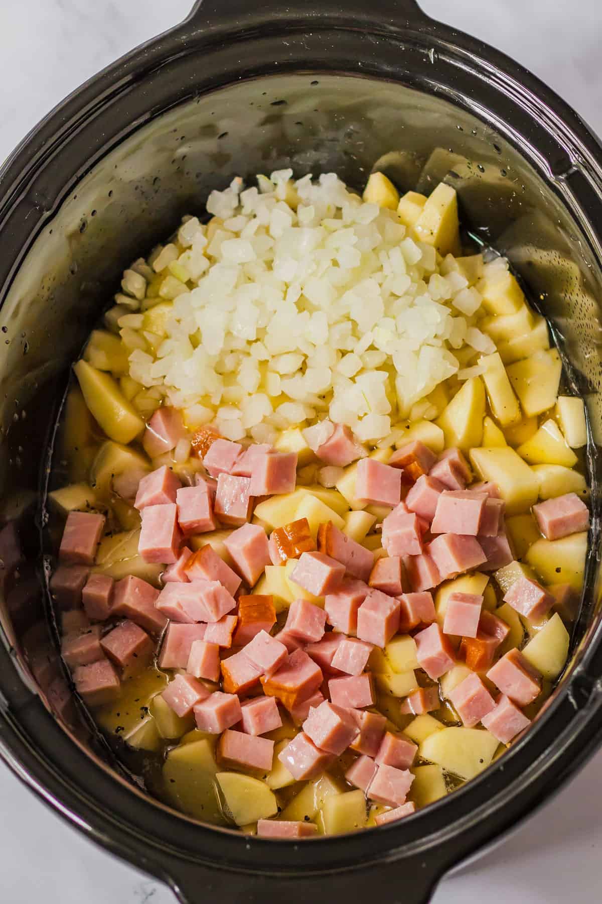 adding ham to a potato soup in the crockpot.