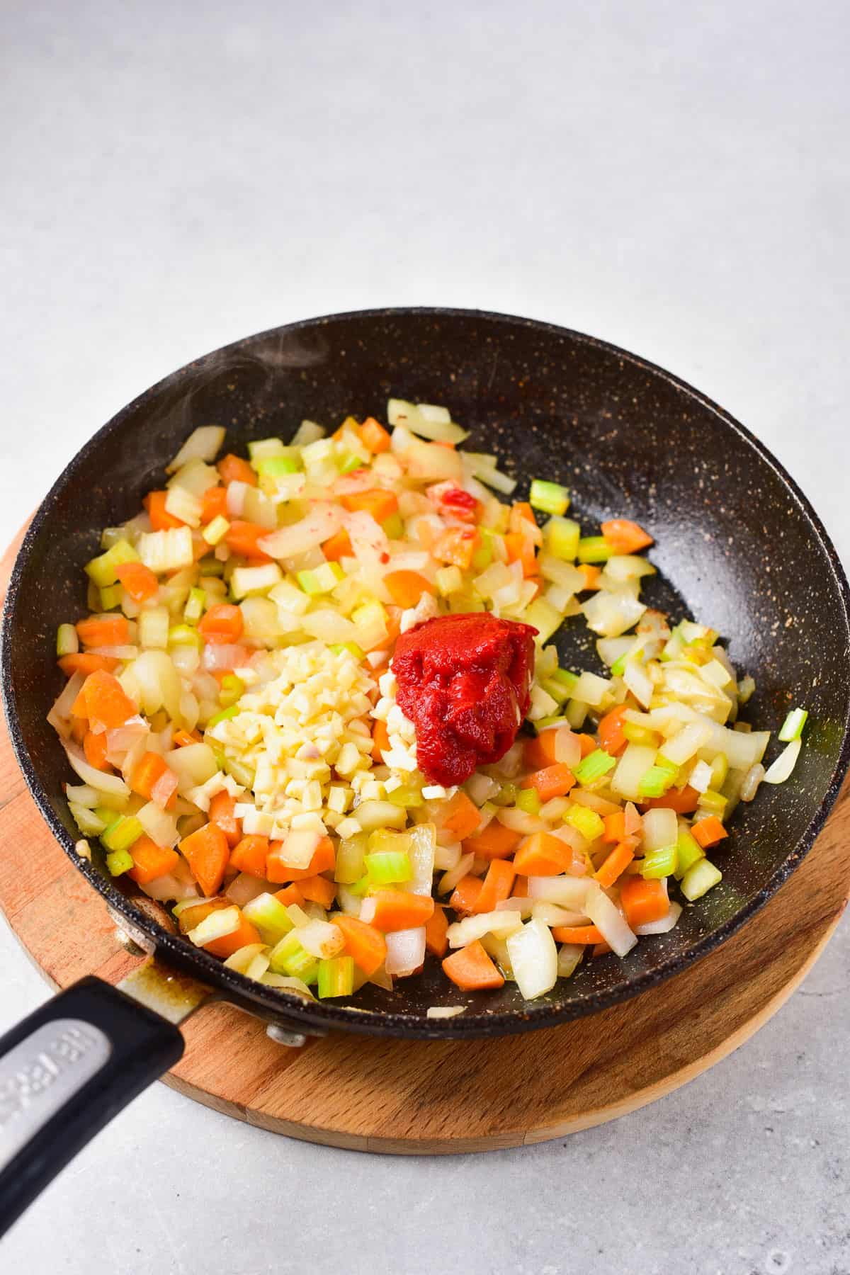 adding tomato paste and garlic to veggie mixture