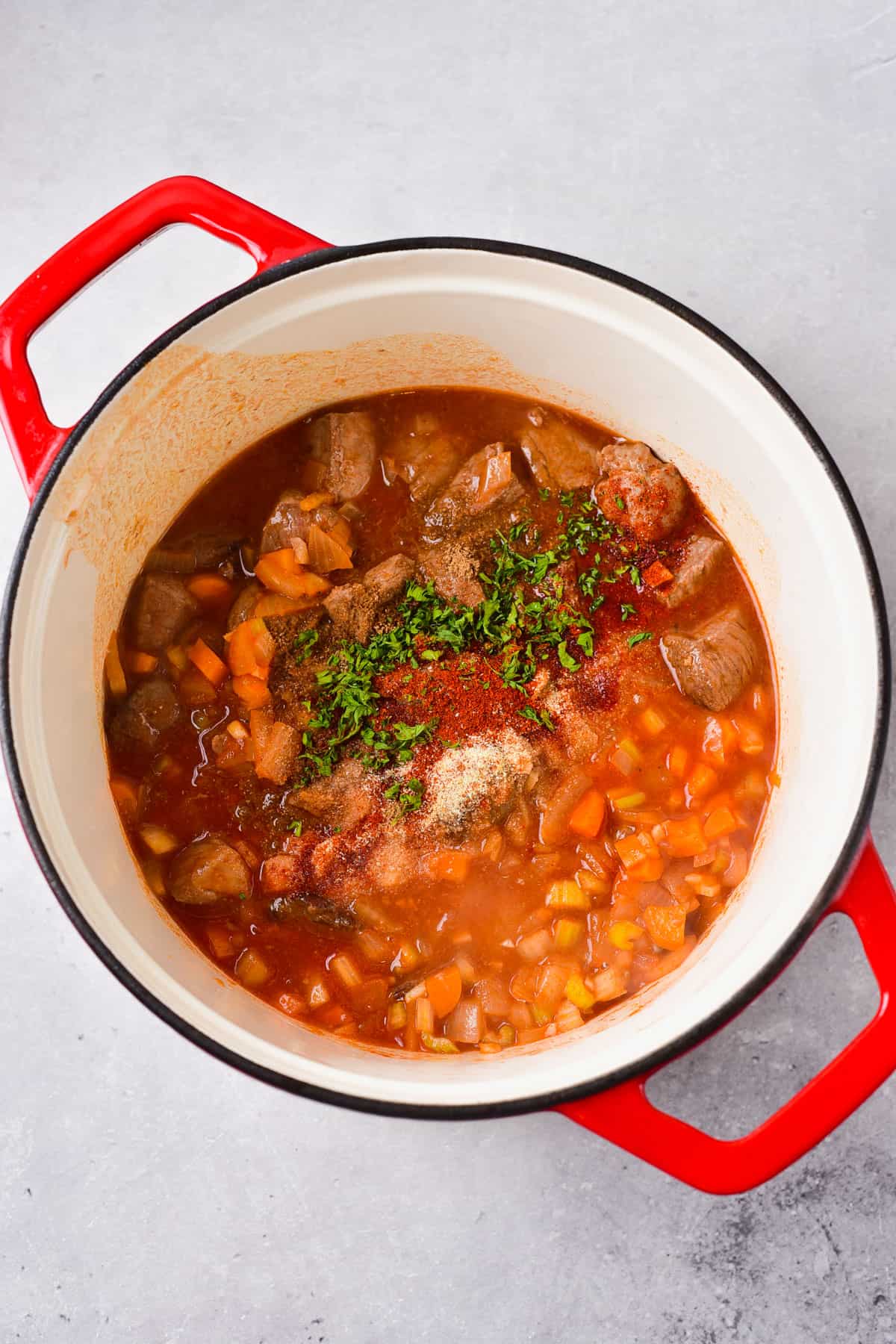 adding more broth and spices to venison stew